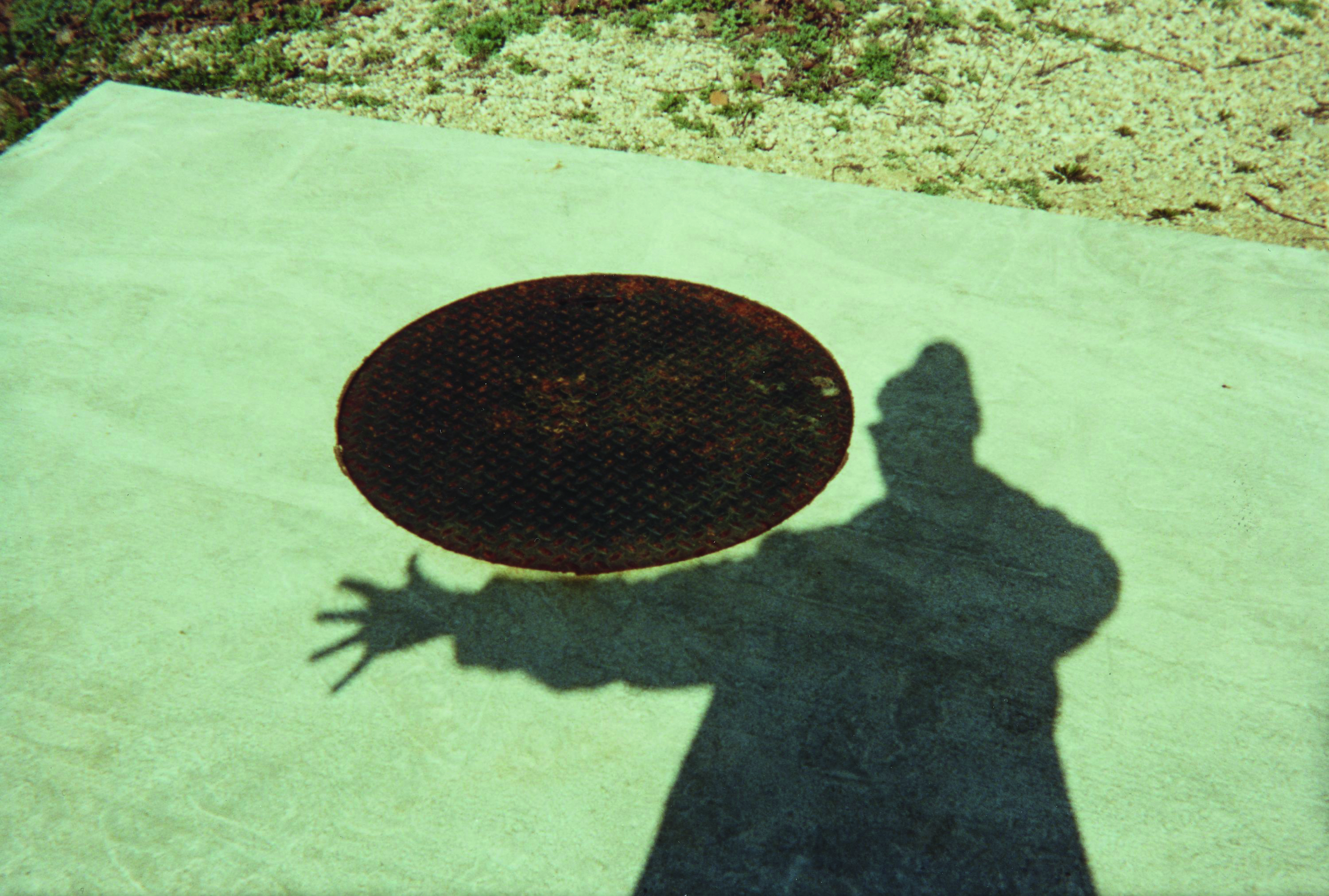 Ray Johnson photo of a man's shadow and a manhole