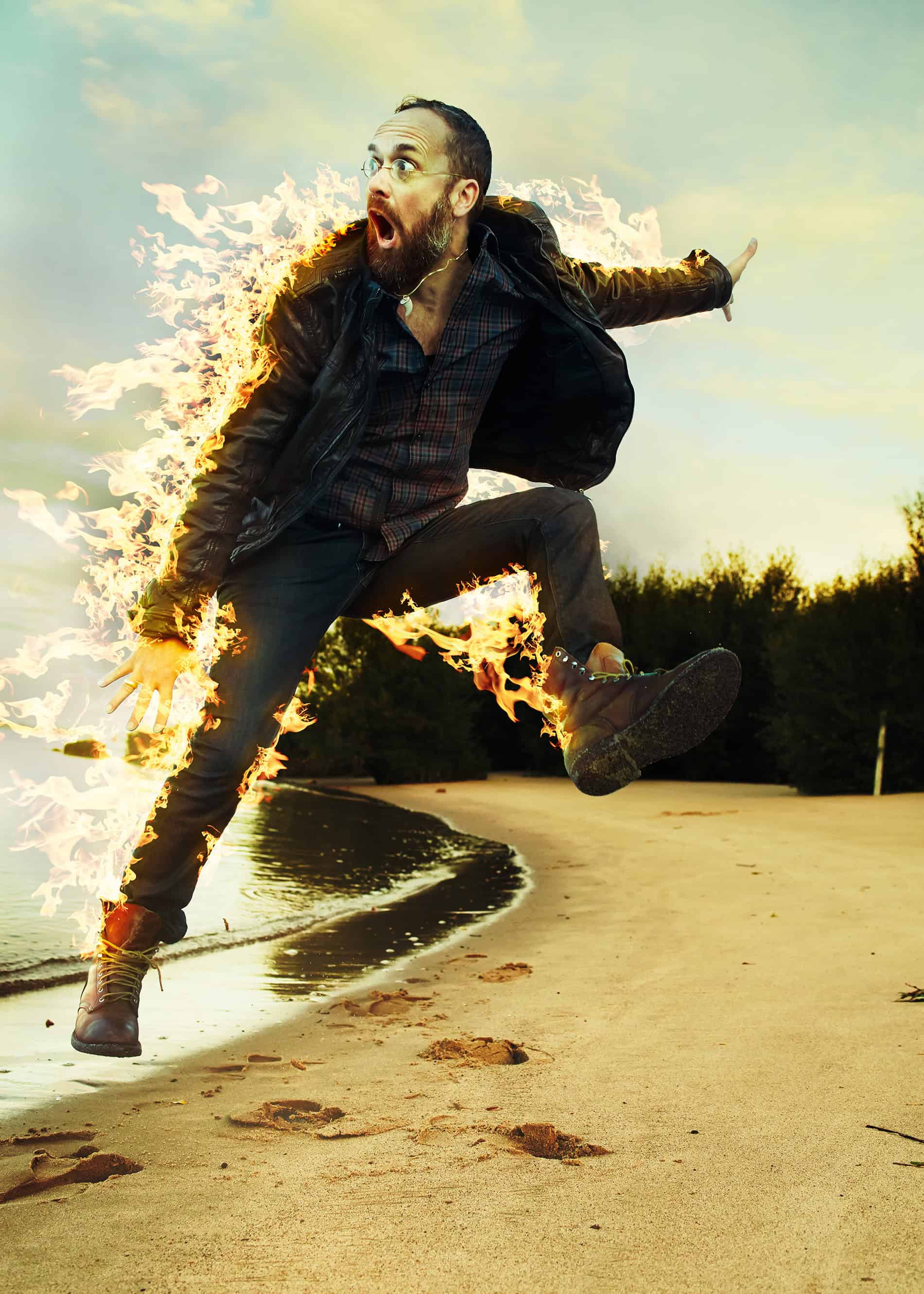 serviceplan's alex schill leaps into the air, his clothes on fire. he is on a sandy beach.