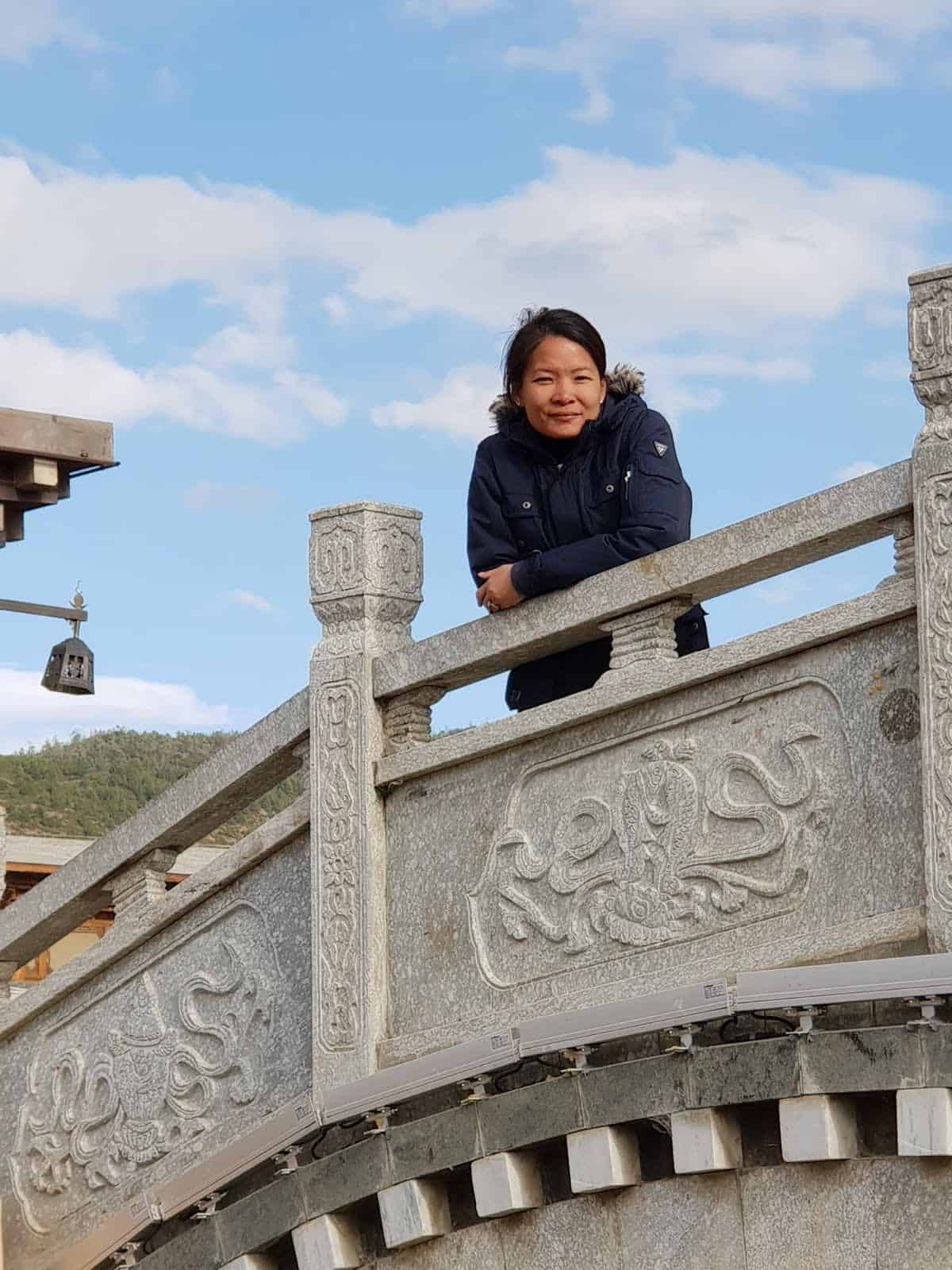 valerie madon, a young east asian woman, stands on a stone bridge looking down at the camera